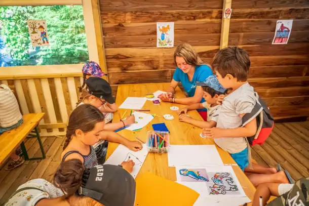 Atelier de dessin et de coloriage dans un espace en bois chaleureux, où des enfants, encadrés par une animatrice dessinent 